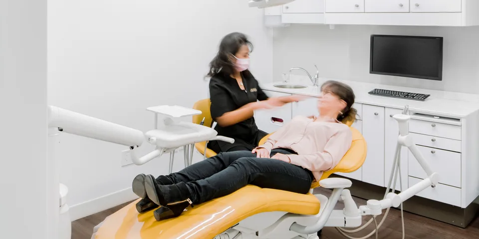 Salle de soins blanche avec fauteuil jaune, une personne allongée et une personne masquée à ses côtés.