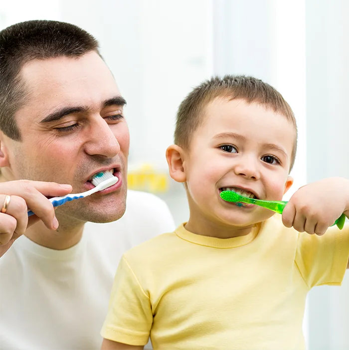 An adult and a child brushing their teeth together